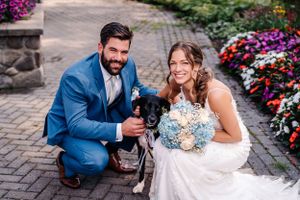 Wedding couple poses with their black dog among colorful flower gardens on stone patio.