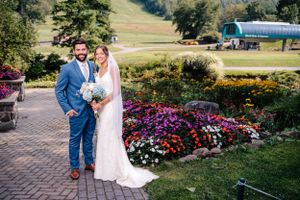 Elegant wedding photo on stone pathway with colorful flower gardens and mountain landscape.
