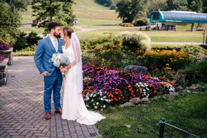 Intimate wedding moment captured on stone path with colorful garden flowers and mountain backdrop.