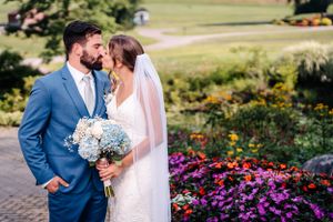 Romantic wedding portrait with blue hydrangea bouquet against garden backdrop.