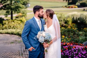 Intimate wedding moment with light blue bouquet against colorful garden setting.