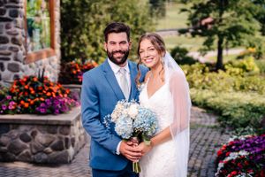 Garden wedding portrait with stone wall and vibrant flower beds in background.