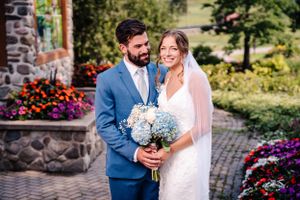 Joyful wedding photo against stone wall with bright floral gardens and mountain views.