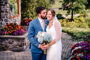 Newlyweds share an intimate moment among vibrant flower gardens while holding a blue and white bouquet.