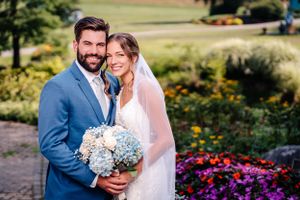 Joyful wedding portrait outdoors with bright floral landscaping and rolling hills in background.