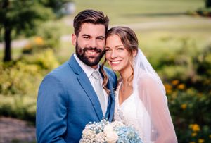Wedding couple smiles brightly for portrait surrounded by lush summer garden scenery.