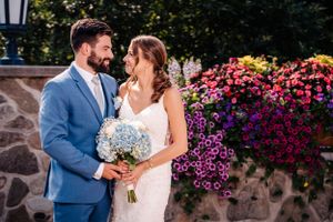 Tender moment between newlyweds by stone wall with cascading purple flowers.