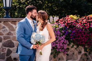 A couple shares an intimate moment in front of vibrant pink flowers and a stone wall on their wedding day.