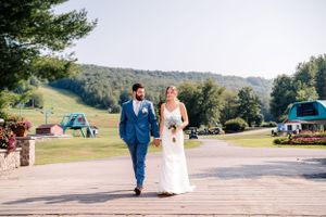 A wedding couple walks together on a scenic mountain path with rolling hills in the background.