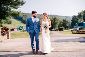 A newlywed couple walks hand in hand on a scenic mountain resort pathway.