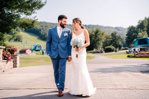 A wedding couple takes a romantic walk outdoors with mountains and trees in the background.