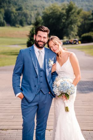 Newlyweds share intimate moment outdoors with blue hydrangea bouquet against mountain landscape.