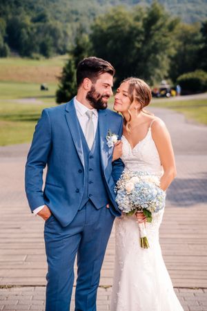 Romantic wedding portrait with couple in blue suit and white dress holding hydrangea bouquet.