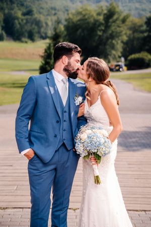 Intimate wedding moment captured outdoors with couple in classic blue suit and white gown.
