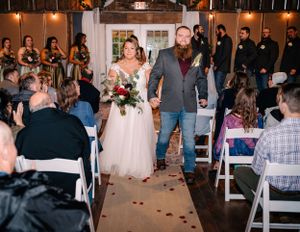A joyful wedding ceremony exit with guests seated in white chairs as the couple walks down the flower-lined aisle.