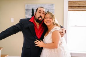Playful wedding portrait with navy suit and white dress against neutral wall.