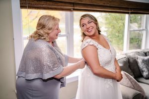 Sweet getting ready moment as final wedding dress adjustments are made by window light.