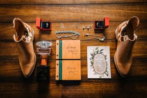 Wedding details flatlay with brown boots, rings, stationery and decorative elements on wooden background.