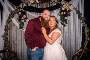 Romantic portrait under floral arch with burgundy and white wedding attire.