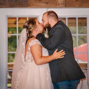Sweet kiss moment between couple in formal wedding attire by window.