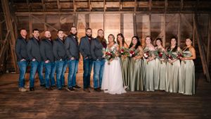 Wedding party poses in rustic barn with bridesmaids in sage green dresses and groomsmen in navy.