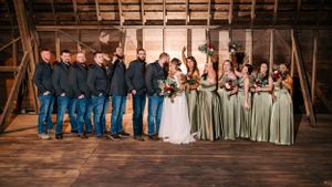 Wedding party lineup in a rustic wooden barn with sage green bridesmaid dresses.