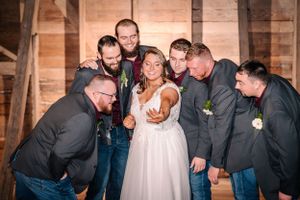 Wedding party gathers around bride for fun photo in rustic barn setting.
