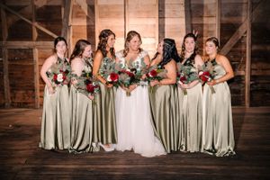 Bridal party poses in sage green bridesmaid dresses and white wedding gown inside rustic wooden venue.