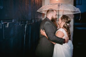 Romantic nighttime portrait under clear umbrella in formal wedding attire.