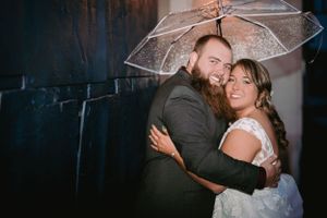 Evening wedding portrait with couple embracing under clear umbrella.