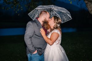 A couple shares an intimate moment under a transparent umbrella in an evening garden.
