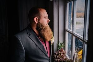 Side profile portrait of person with red beard wearing dark blazer looking out window.