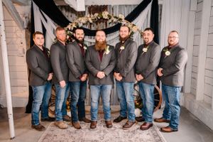 Group photo of groomsmen in matching grey blazers and jeans against industrial backdrop.