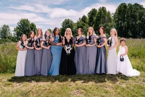 Wedding party in mixed gray and blue dresses pose together in a sunny meadow.