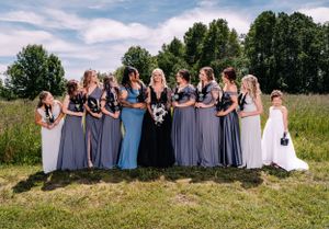 Bridesmaids in various shades of blue and gray dresses stand together for a group photo outdoors.