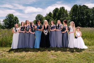 Wedding party lined up in coordinating blue and gray dresses against a natural meadow backdrop.