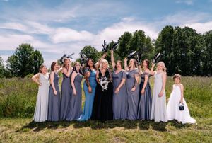 Bridal party in mixed gray dresses poses playfully in a summer field.