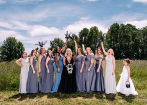 Wedding party raises their arms in celebration while posing for a group photo outdoors.