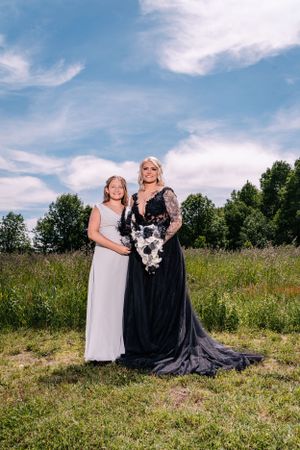 A formal portrait in a meadow featuring a black wedding gown and white dress.