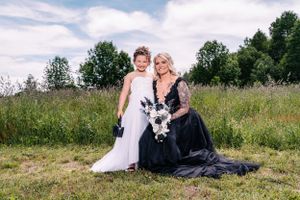 Two people pose together in a sunny field wearing matching black and white formal dresses.