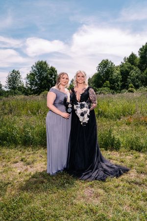 Two people in formal attire pose with a black and white bouquet against a backdrop of summer greenery.
