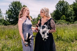 Two people in formal attire share a candid moment while holding bouquets in an outdoor setting.