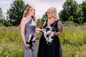 Two women in formal gowns share a candid moment in a sunny wildflower meadow.