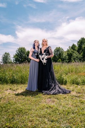 A dramatic portrait of two women in contrasting gowns standing in a summer field.