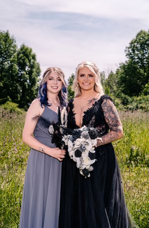 Two wedding party members pose with white floral arrangements in a summer meadow.