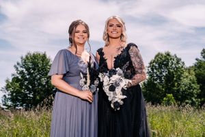 Two attendants in contrasting formal gowns pose in a sunlit summer field.