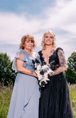 Two people share a tender moment while wearing formal gowns in an outdoor setting.