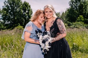 Two people embrace emotionally while holding a white floral bouquet in a summer meadow.