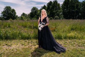 Person wearing dramatic black lace gown poses with bouquet in wildflower field.
