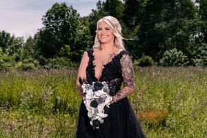 Person in flowing black gown with lace details poses elegantly in summer field.